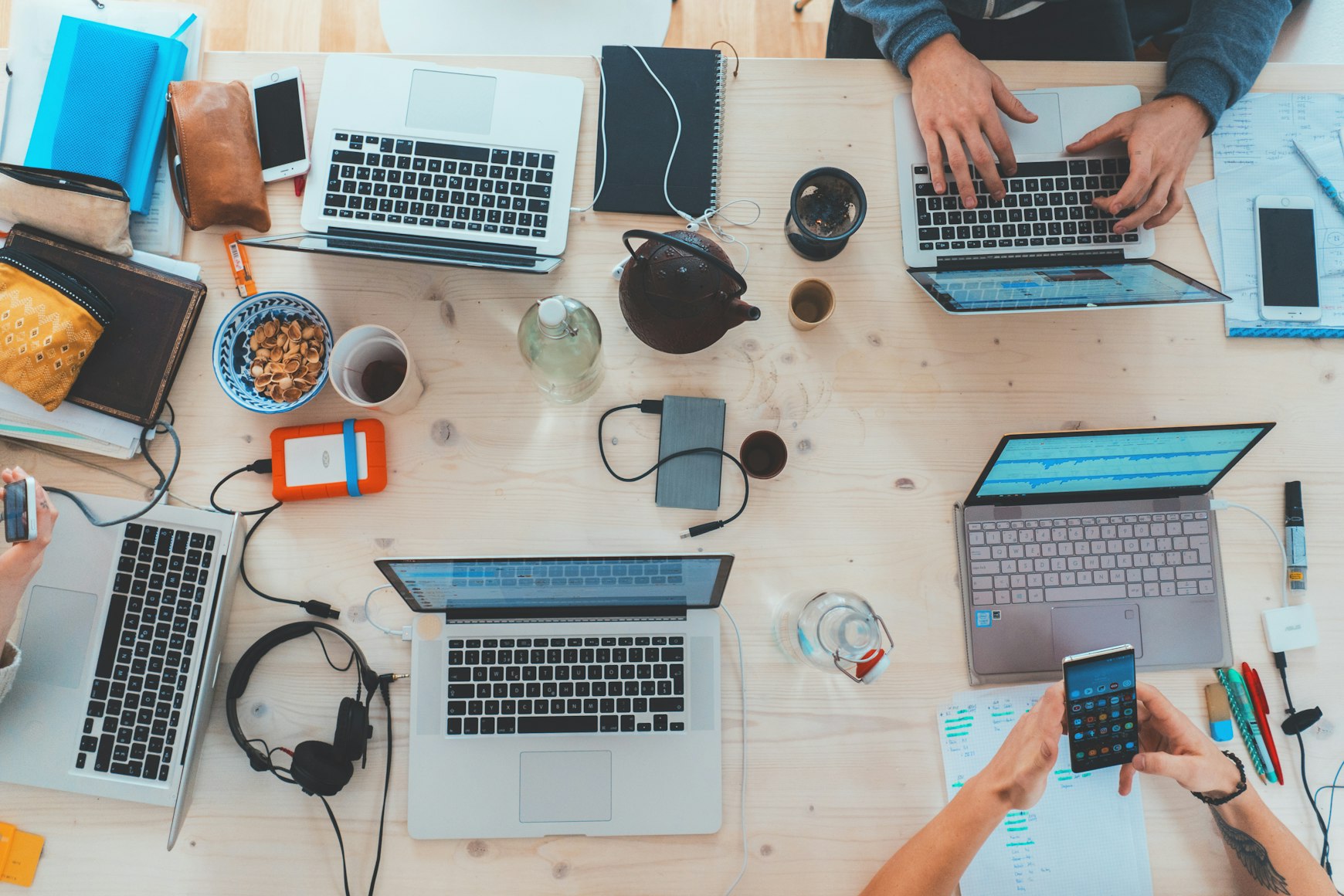 Echipă lucrând împreună la o masă cu laptopuri și telefoane